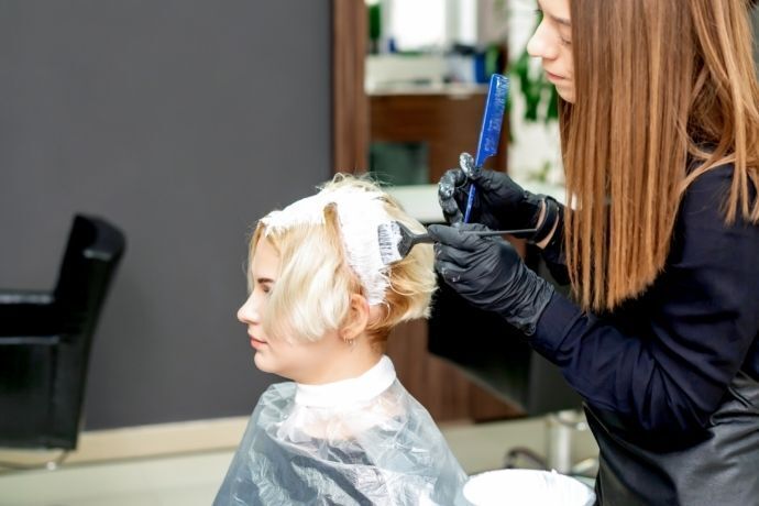 Pessoa pintando o cabelo de mulher de loiro claro