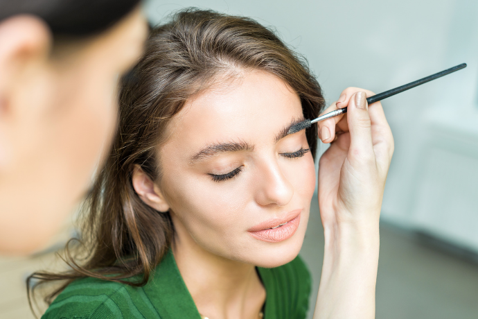 Profissional aplicando tinta em sobrancelha de mulher.