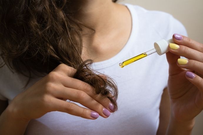 Mulher com conta gotas aplicando óleo no cabelo