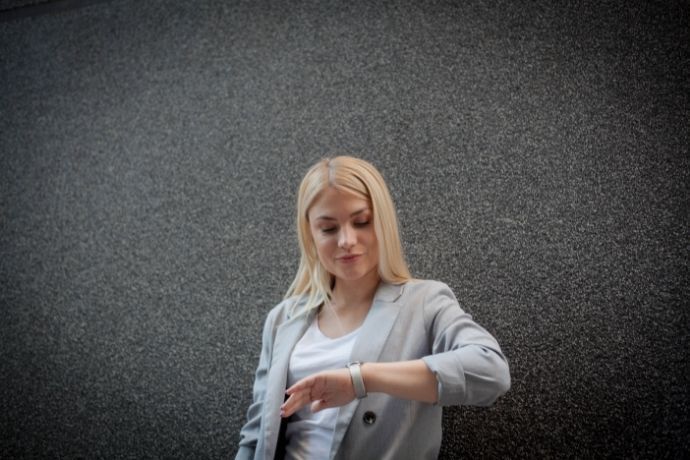 Mulher olhando horas em relógio em fundo cinza