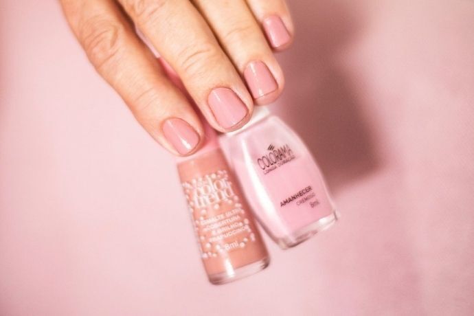 Dedos com unhas pintadas de uma cor clara segurando duas embalagens de esmaltes