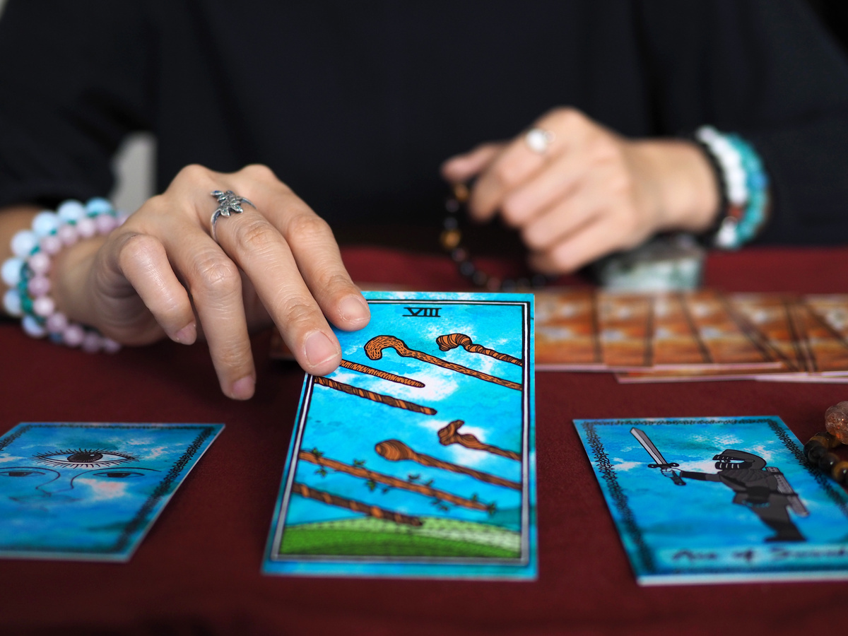 Mulher segurando a carta 8 de Paus do Tarot sobre mesa de veludo vermelho.