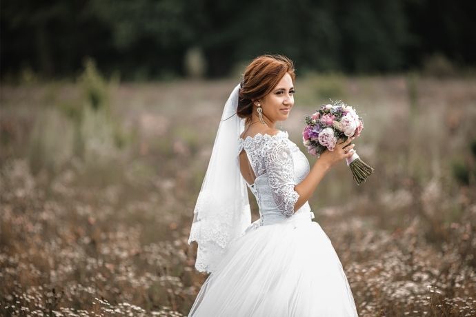 Mulher vestida de noiva segurando um buquê em um gramado