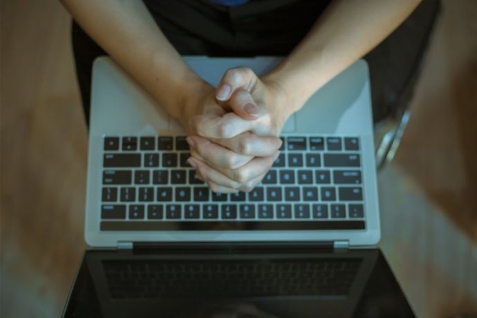 Pessoa com mãos em sinal de oração em cima de notebook