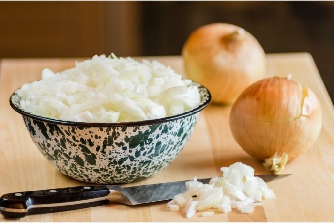 Cebola picada em pote e duas cebolas e faca ao lado