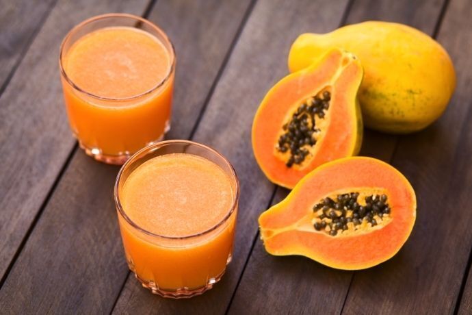 dois copos com suco de mamão ao lado de mamões