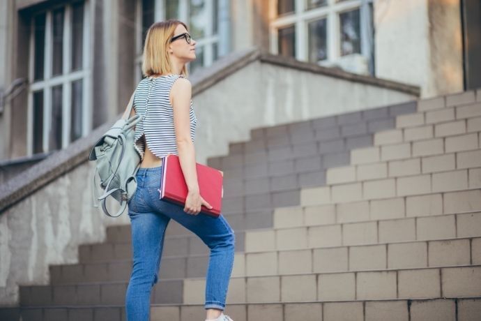 Mulher com mochila e livro na mão subindo escada