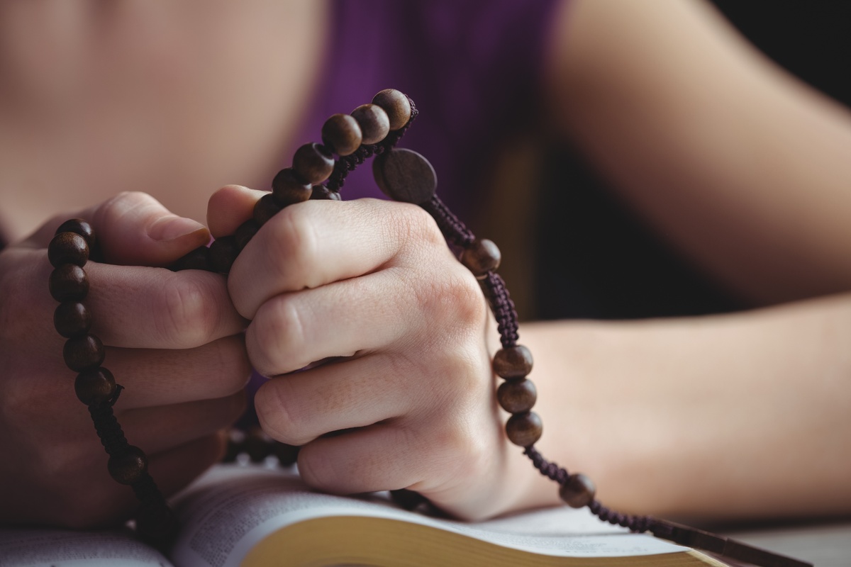 Mãos envolvendo terço, representando as orações que podem ser feitas para trazer calma durante um episódio de paralisia do sono.