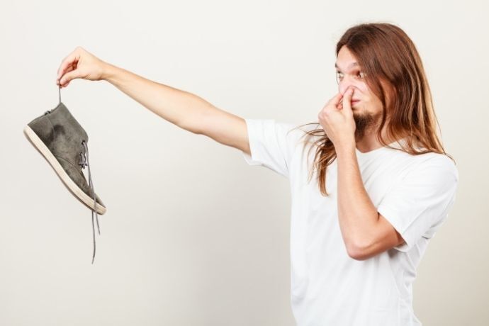 Pessoa segurando sapato e cobrindo o nariz com as mãos