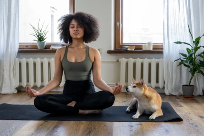 Mulher meditando em tapete ao lado de cachorro