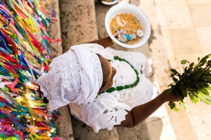 Mulher com roupas brancas segurando ramo de folhas em frente a Igreja de Senhor do Bonfim