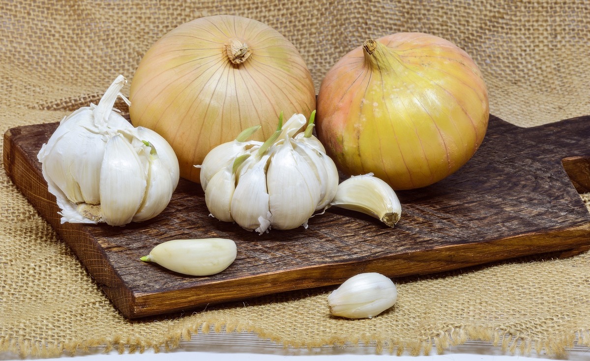 Cebolas amarelas juntas de cabeças de alho abertas em tábua de madeira.