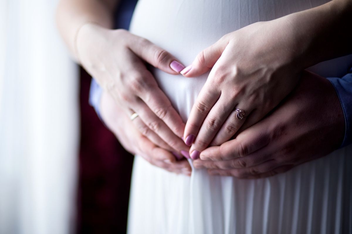 Casal com mãos sobre barriga de mulher.