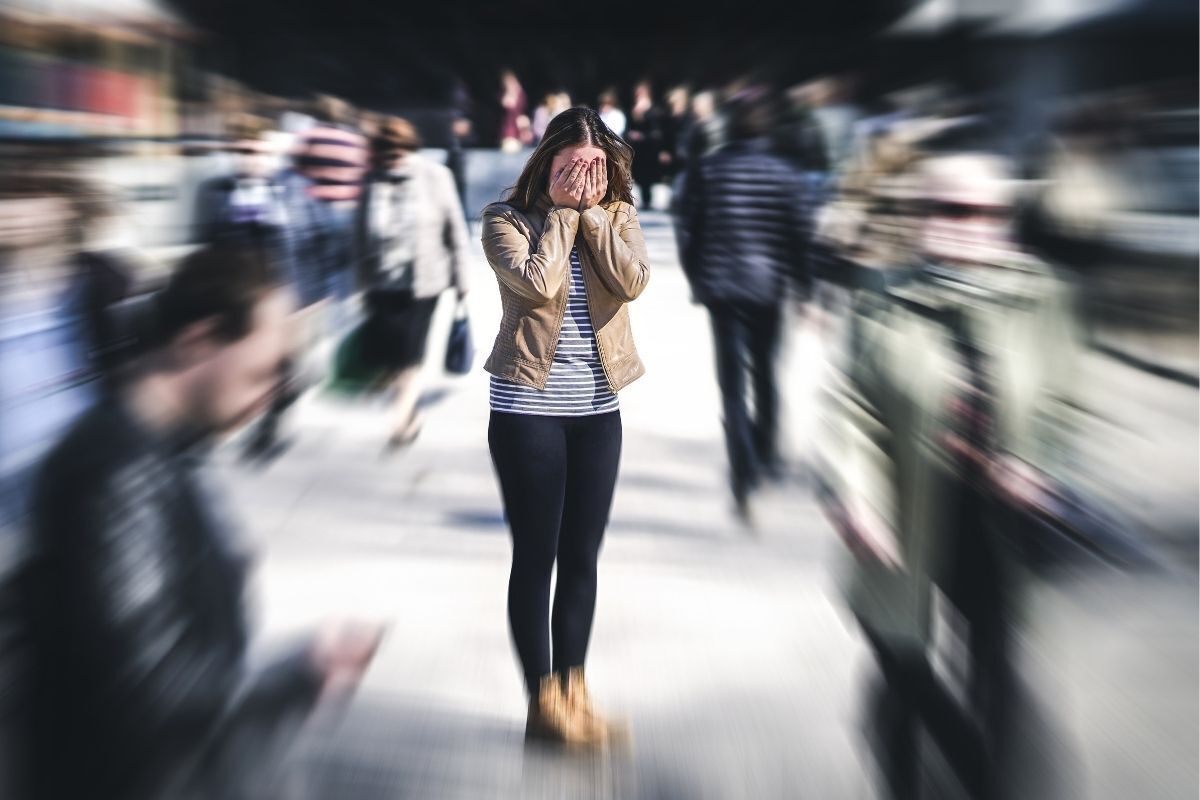 Mulher em crise de ansiedade no meio de rua lotada.