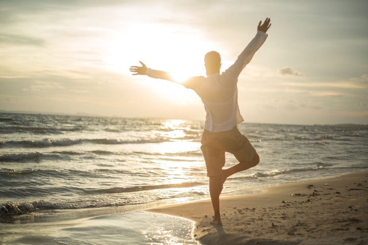 Homem de braços abertos em praia calma.