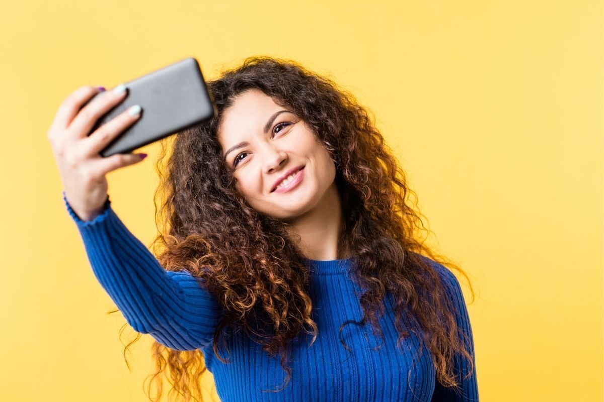 Mulher olhando a própria figura na câmera do celular.