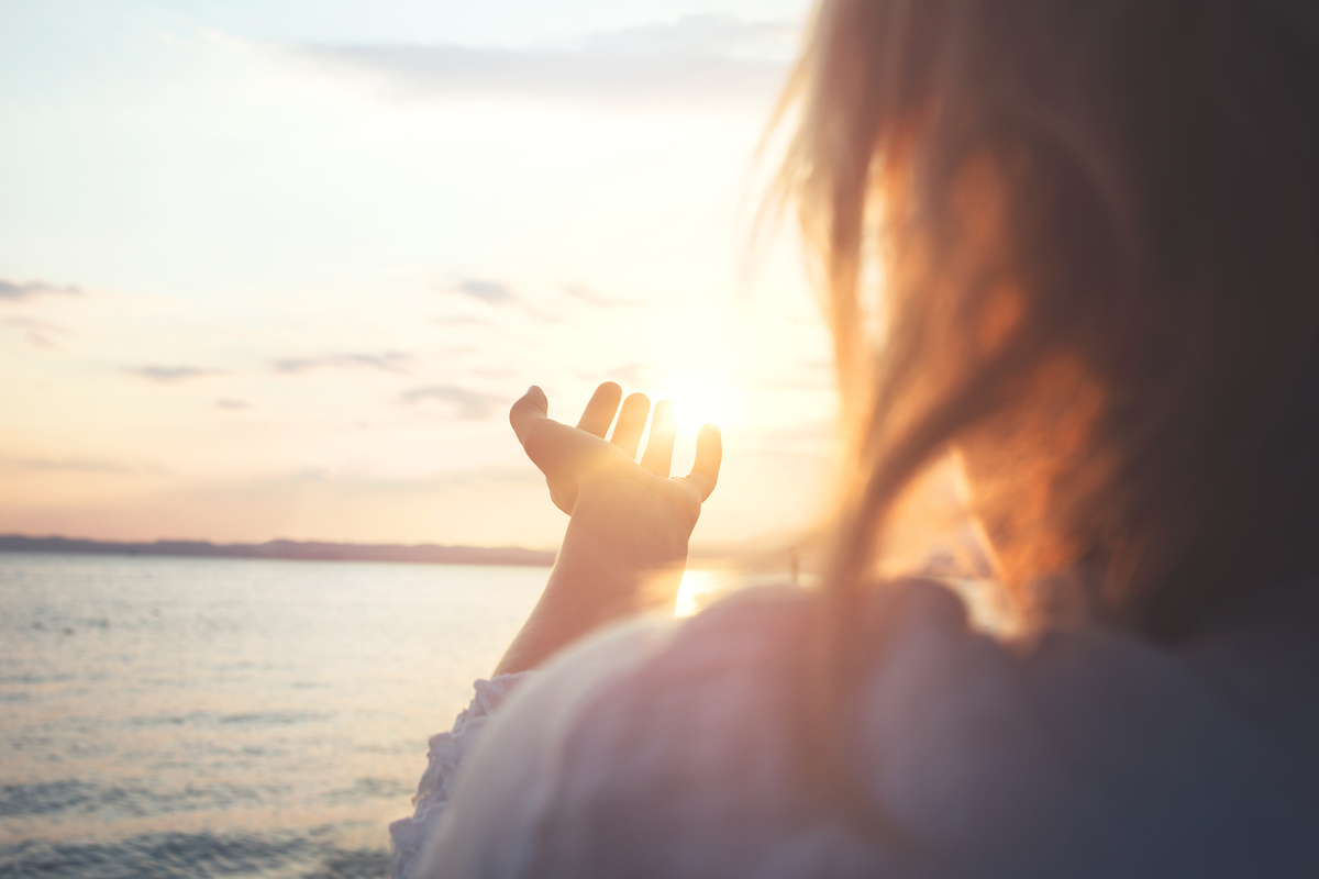 Mulher com mãos em direção ao Sol em agradecimento