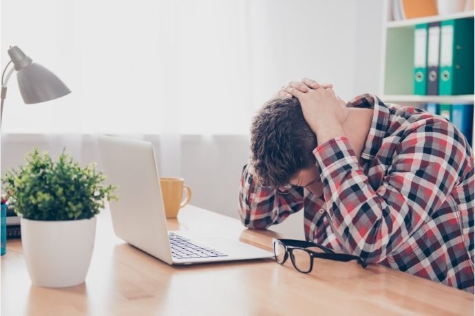 Homem sentado em frente a notebook com as mãos na cabeça