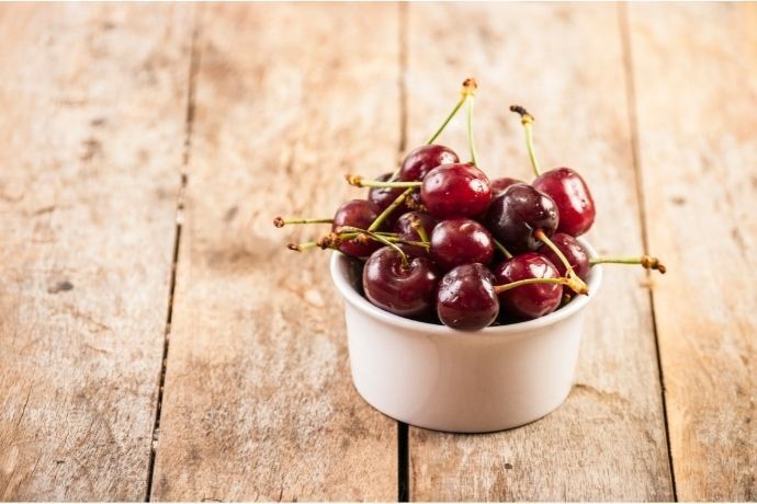 Pequeno pote branco com cerejas em mesa de madeira