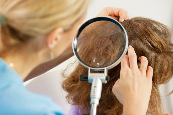 Pessoa procurando piolho em cabelo de outra com uma lupa