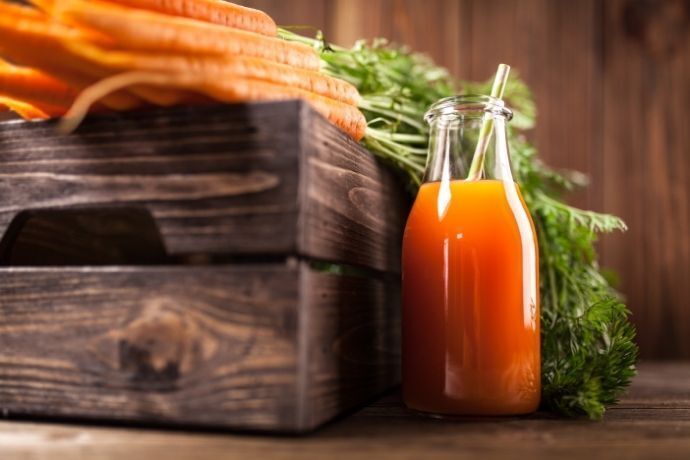 Suco de cenoura ao lado de caixote de madeira com várias cenouras