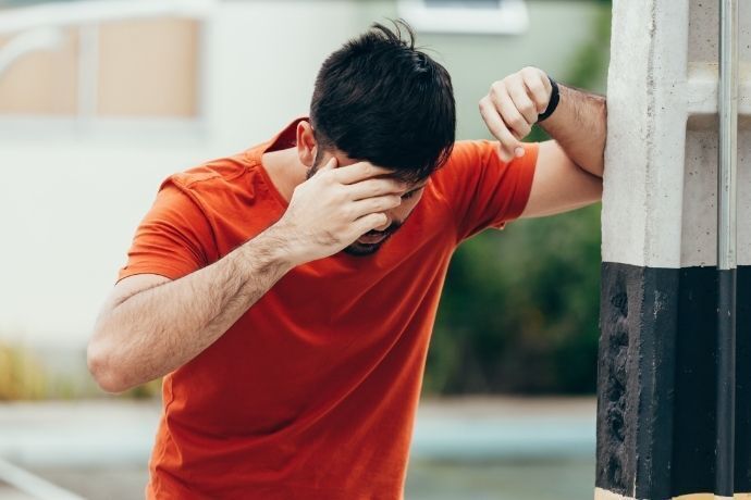 Homem com a cabeça baixa e encostado com tontura