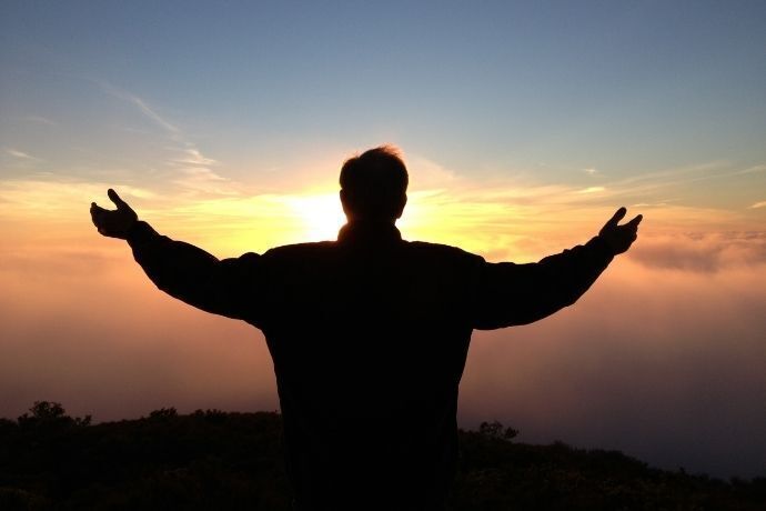 Homem de costas no pôr do sol com braços abertos