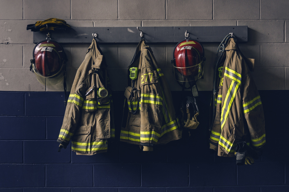 Cabide na parede com casacos e capacetes de bombeiros pendurados.