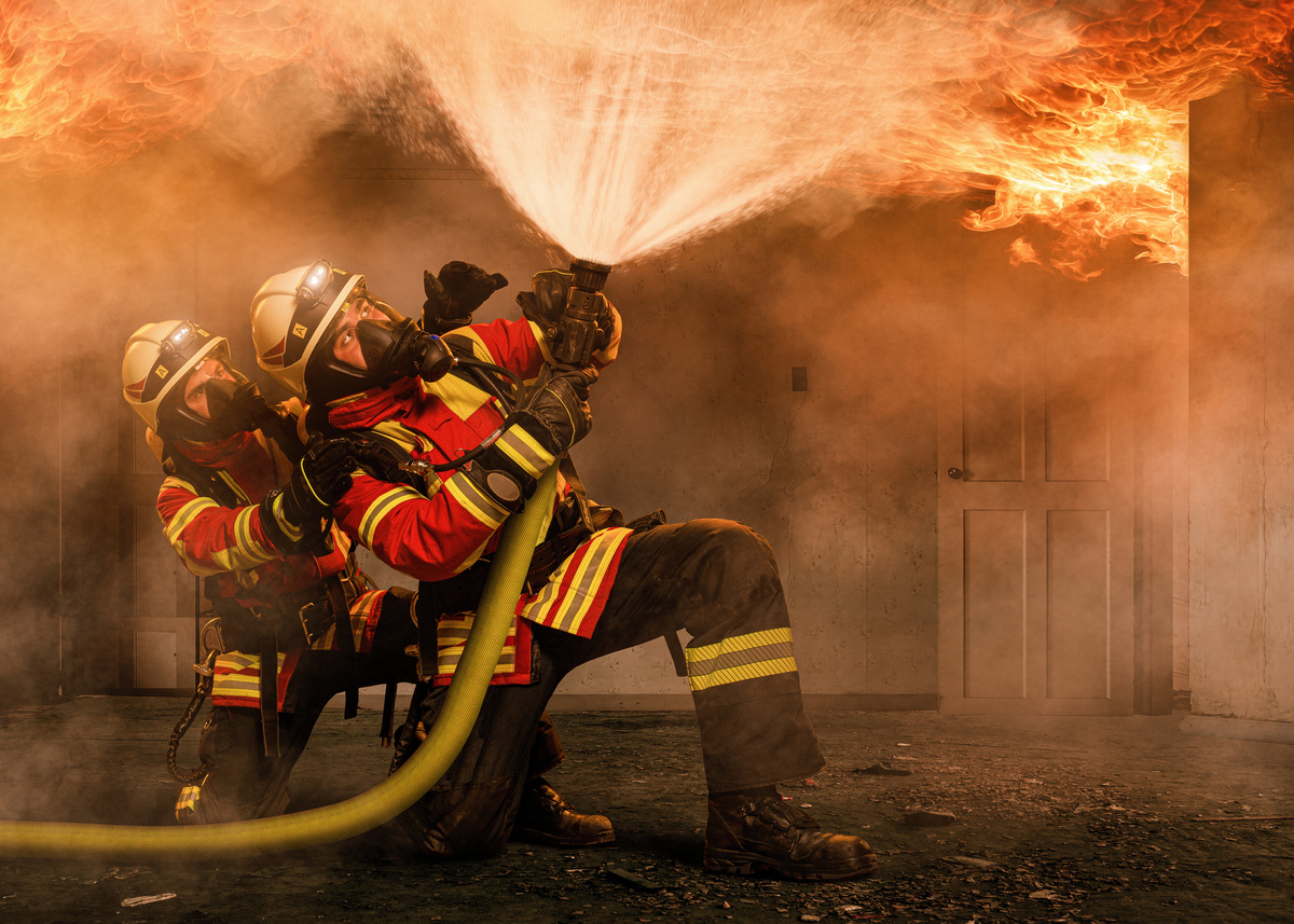 Grupo de bombeiros usando mangueira d'água para apagar fogo.