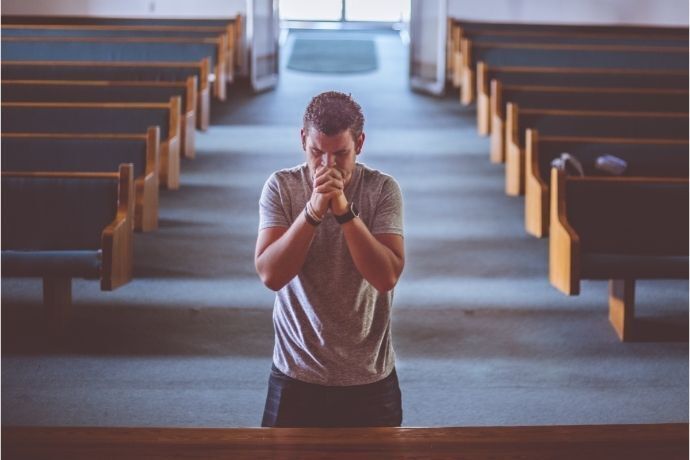 Homem rezando ajoelhado em corredor de igreja