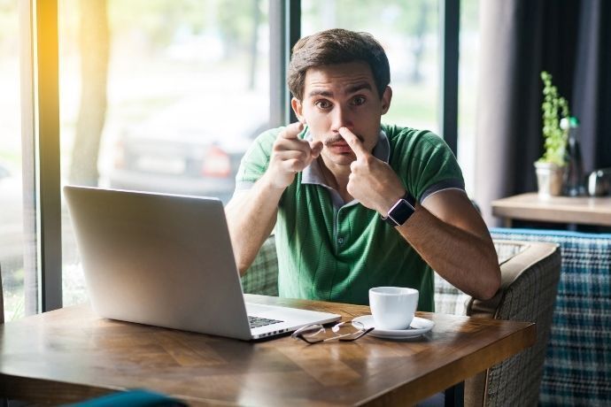 Homem fazendo sinal de falsidade em frente a computador