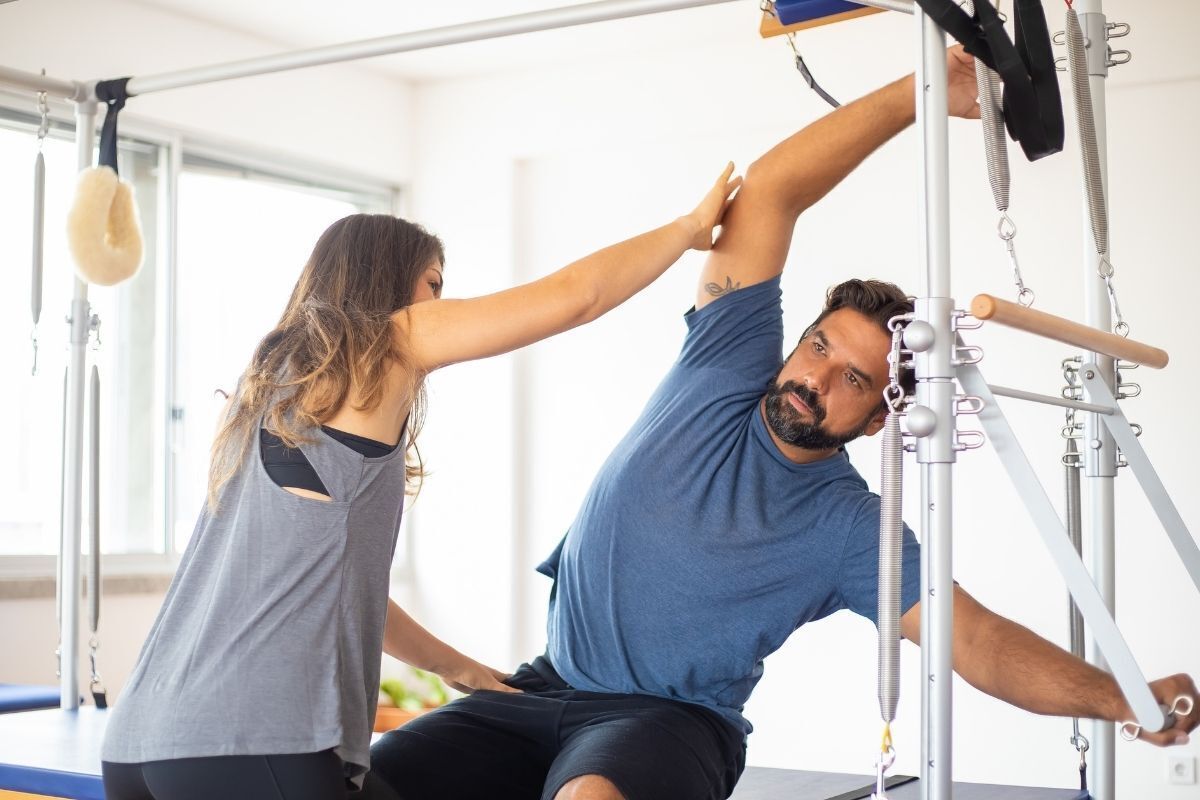 Homem praticando pilates com auxílio.