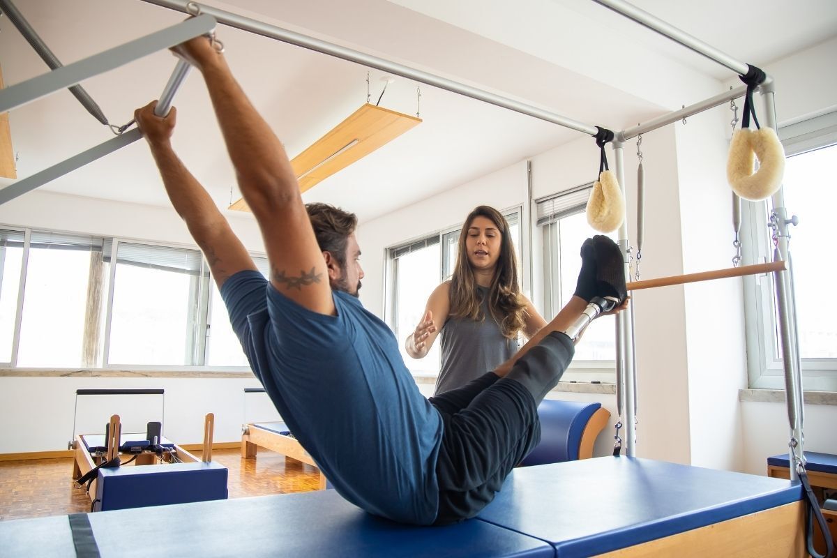 Homem praticando pilates com auxílio.