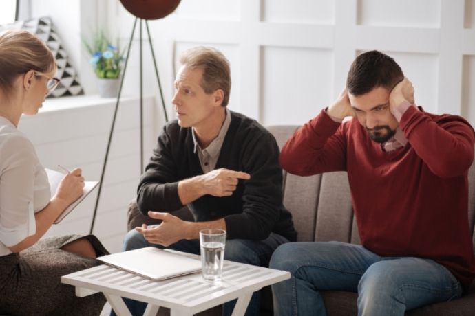 Homens na terapia com um tampando os ouvidos e o outro apontando