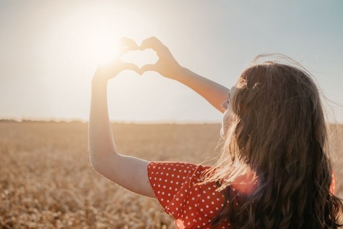 Mulher em campo no sol fazendo coração com as mãos