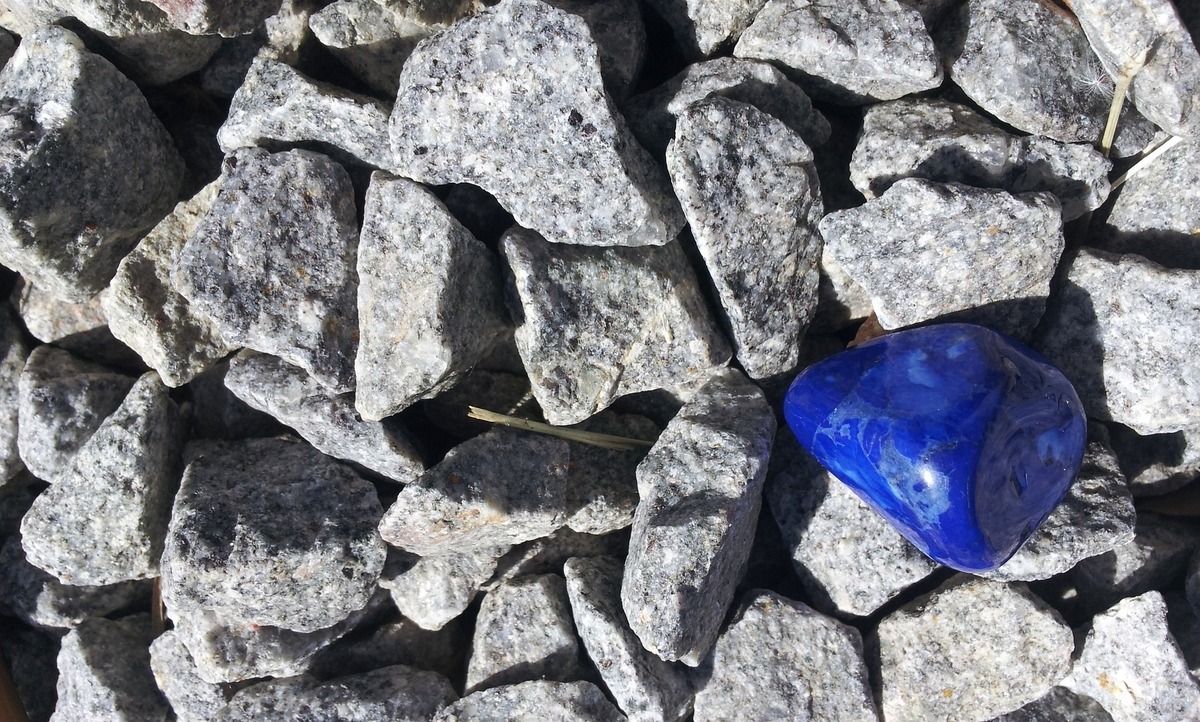 Pedra de Lápis Lazúli em cima de várias outras rochas acinzentadas, se destacando das demais.