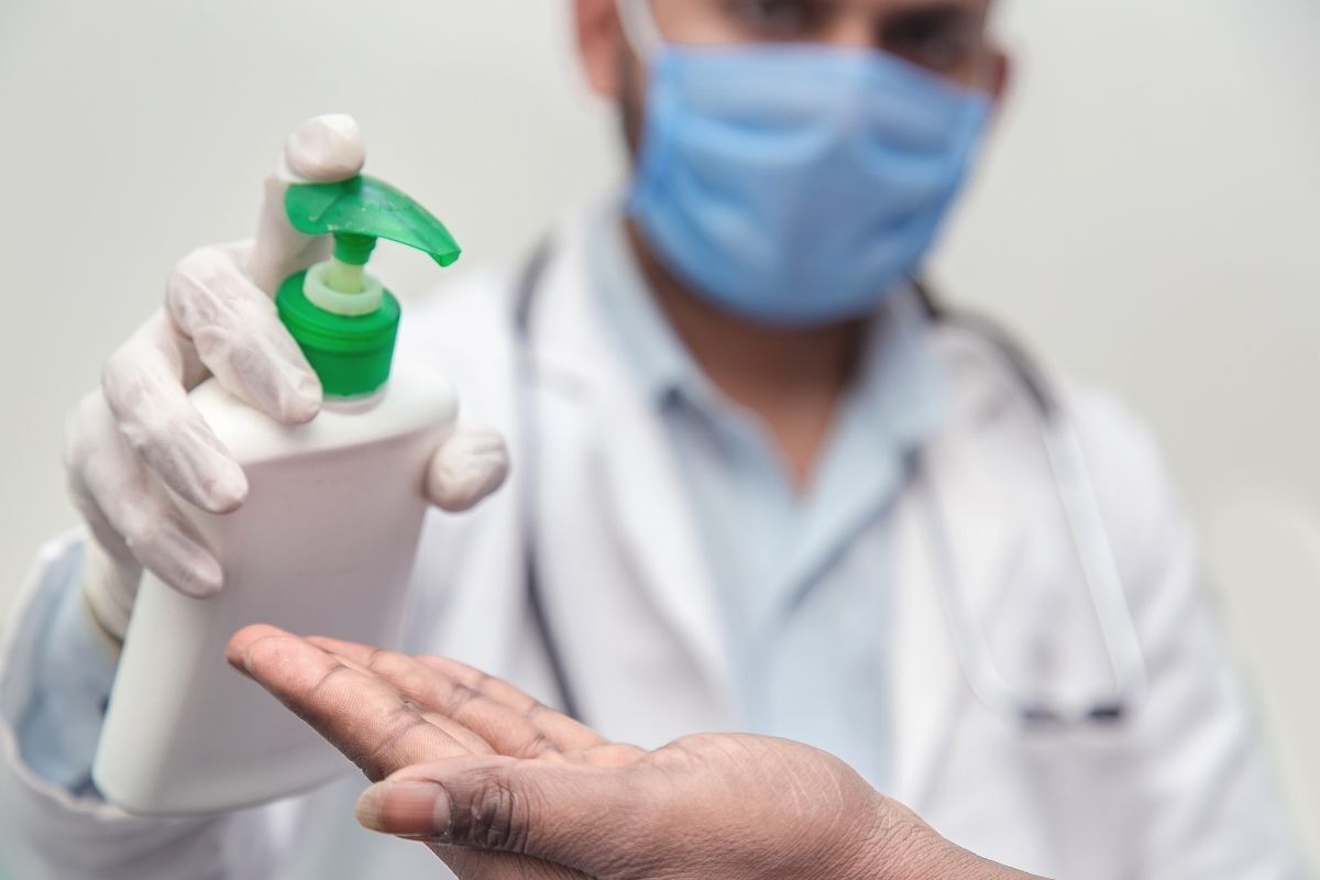 Médico aplicando álcool em gel na mão de paciente.