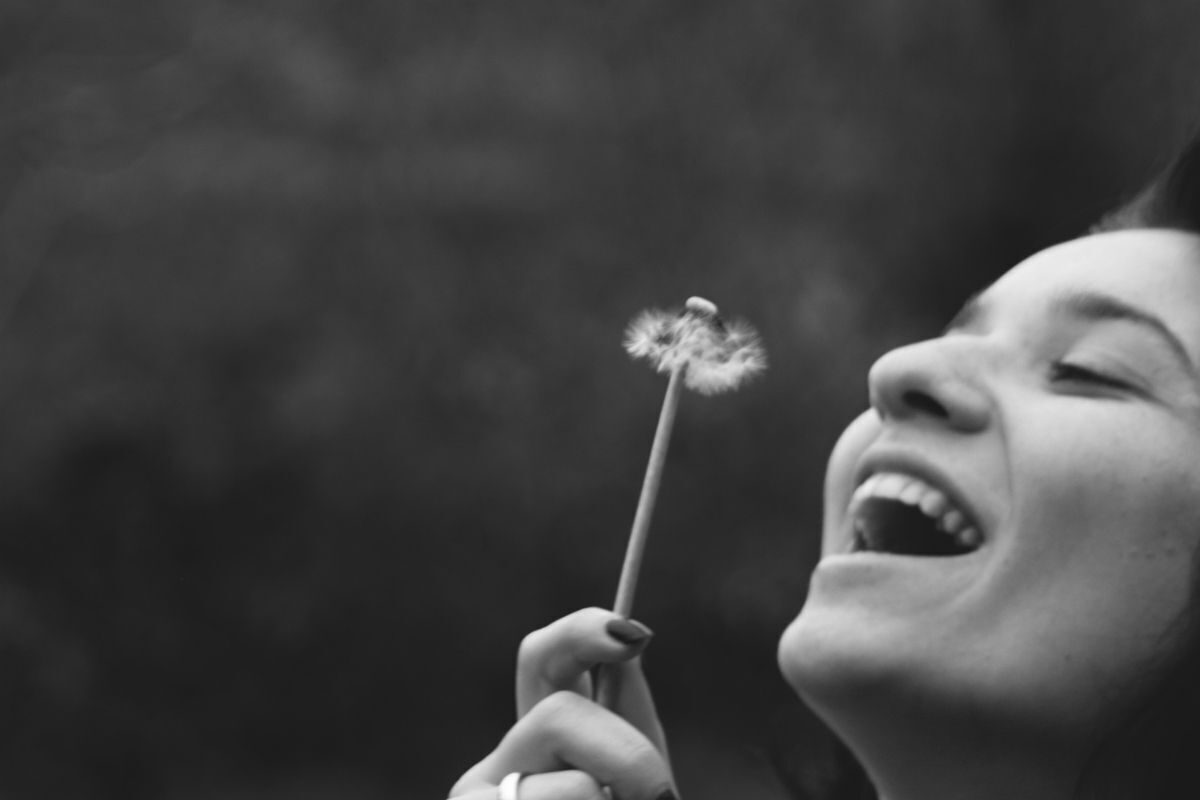 Mulher feliz soprando dente de leão.