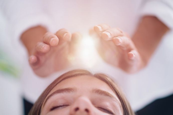 Mulher deitada com pessoa com mãos sobre o chakra coronário