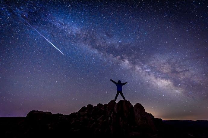 Pessoa de braços abertos e estrela cadente passando em céu estrelado