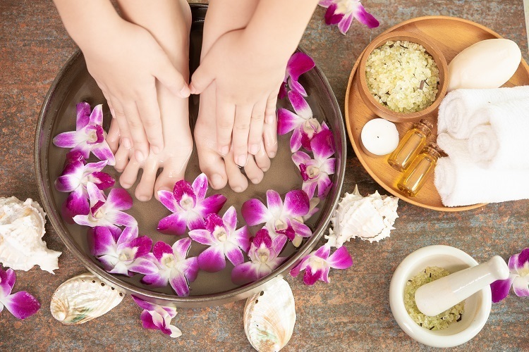 Pés mergulhados em bacia com flores. Ao lado, condimentos para escalda pés. 