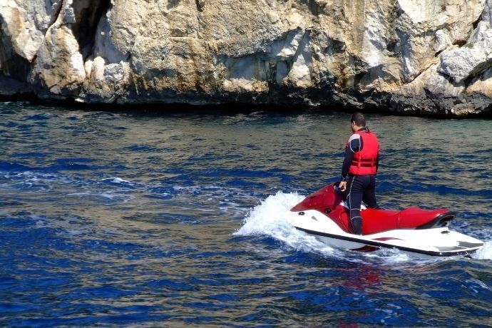 Homem dirigindo jet ski no mar próximo a rochas