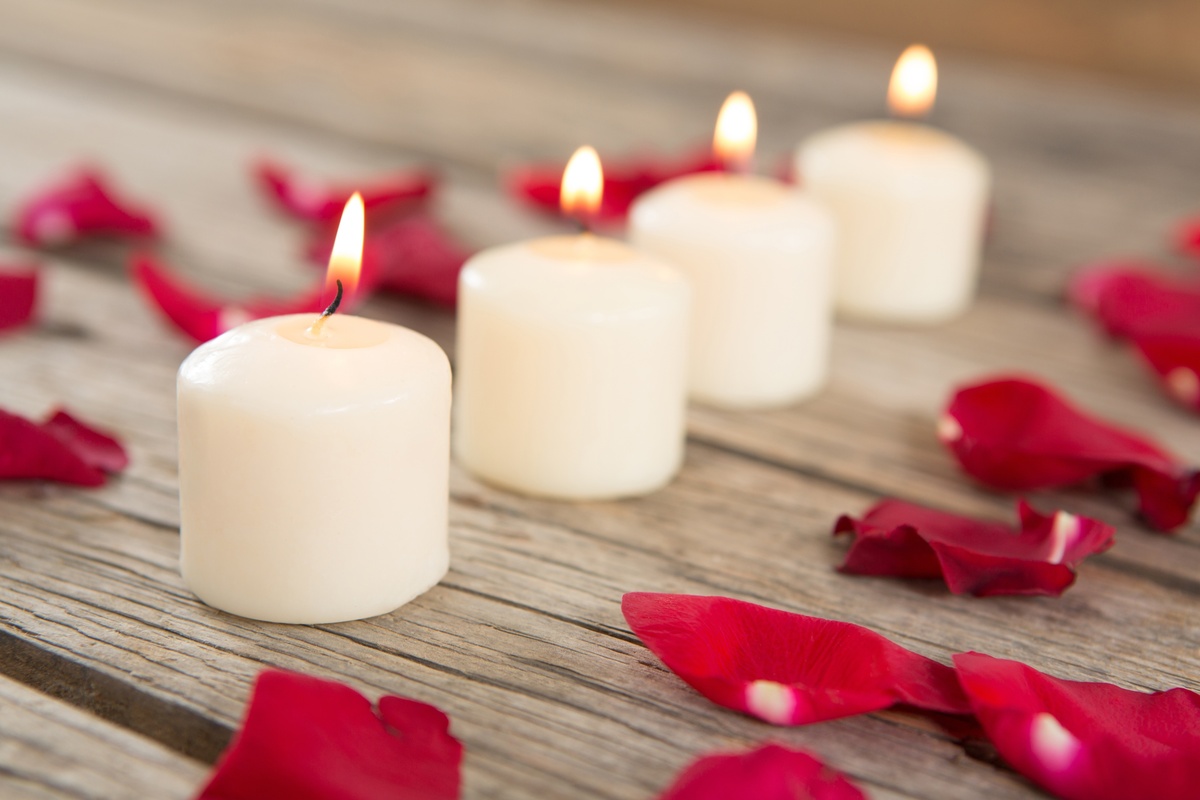 Velas queimando em volta de pétalas de rosas vermelhas.