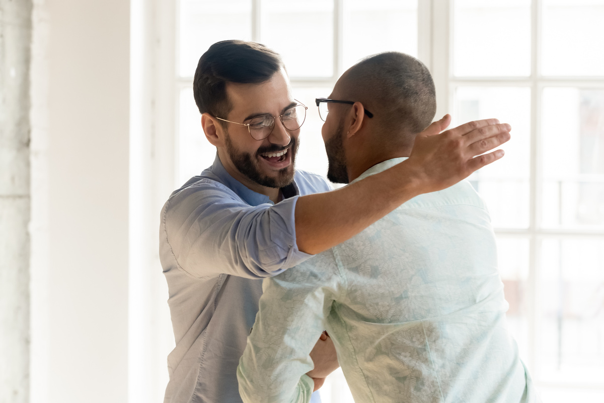 Dois homens se abraçando enquanto sorriem, representando primos se encontrando.