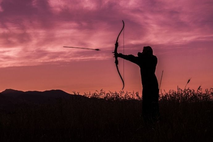 Silhueta de homem apontando uma flecha no pôr do sol