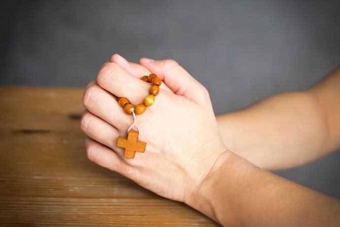 Mãos segurando terço em sinal de oração