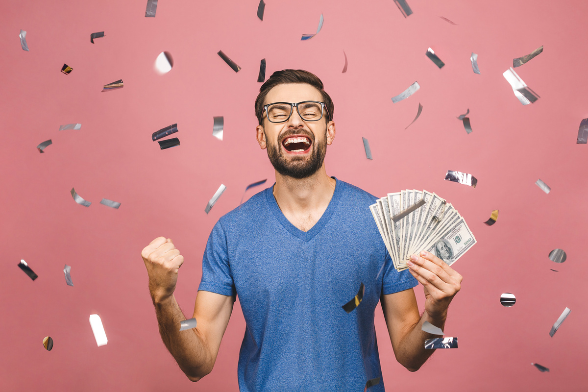 Homem comemorando enquanto segura grande quantidade de dinheiro, representando primo rico.