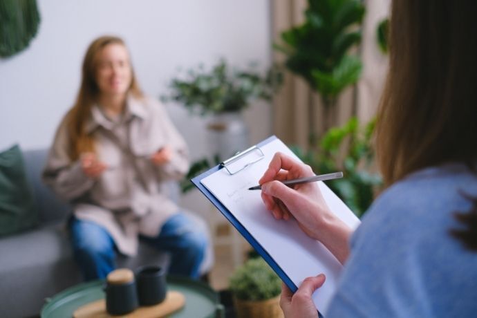 Psicóloga anotando informações enquanto ouve paciente mulher falar