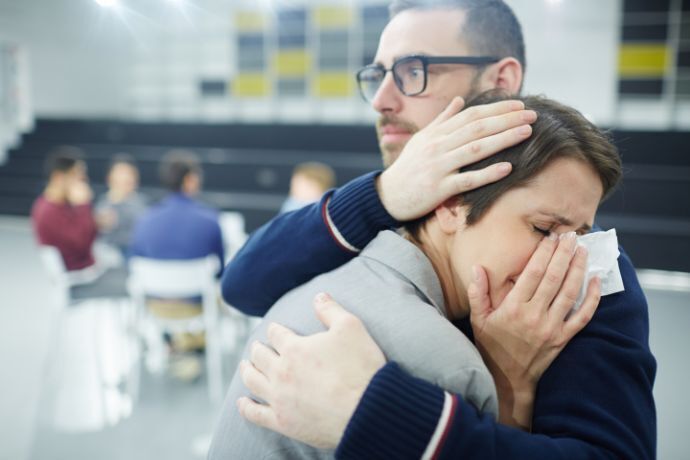 Mulher sendo consolada por homem em grupo de apoio