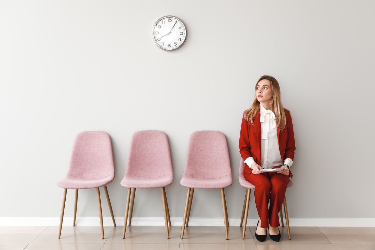 Mulher sentada ao lado de cadeiras vazias, aguardando para ser chamada para sua entrevista de emprego.